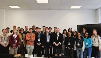 Gruppe von Menschen in einem Konferenzraum, stehen zusammen und lächeln in formeller Kleidung.