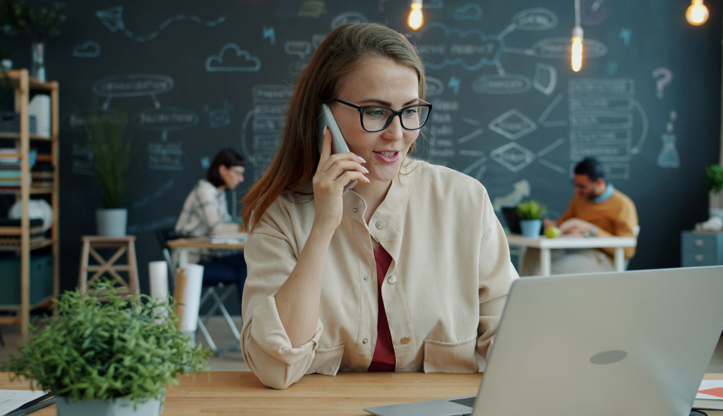A woman talking on the phone at her desk with a laptop